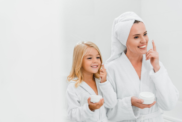 cheerful mother and daughter applying cosmetic cream in bathroom  - Fotoğraf, Görsel