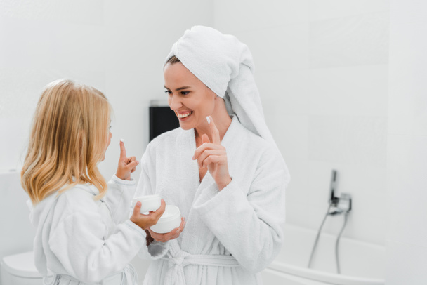 cheerful mother and daughter with face cream on fingers  - Fotografie, Obrázek