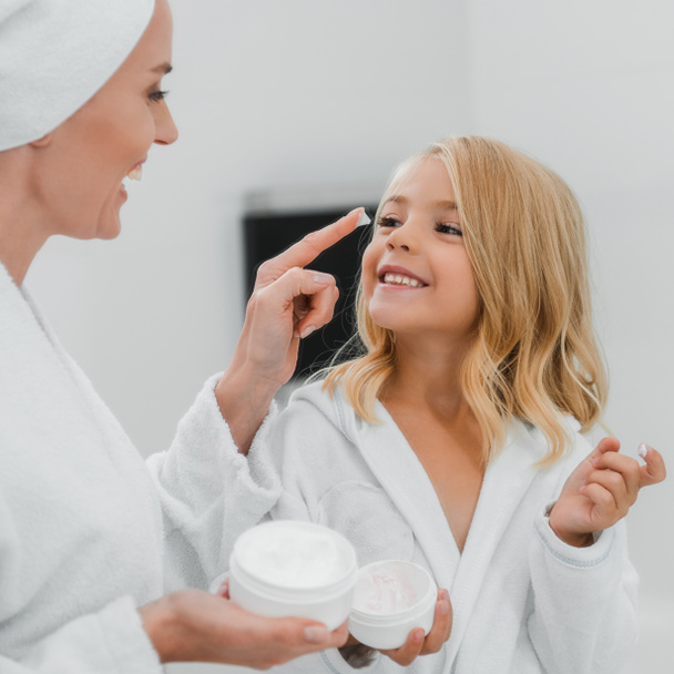 gelukkig moeder het aanbrengen van cosmetische crème op schoon gezicht van dochter  - Foto, afbeelding