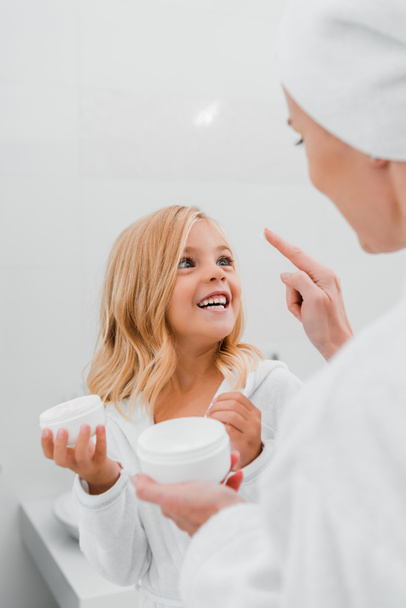 mãe aplicando creme cosmético no rosto limpo da filha feliz
  - Foto, Imagem