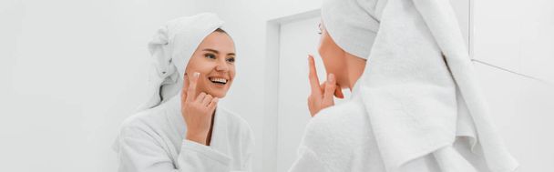 tiro panorámico de la mujer feliz aplicando crema cosmética en la cara limpia
  - Foto, Imagen