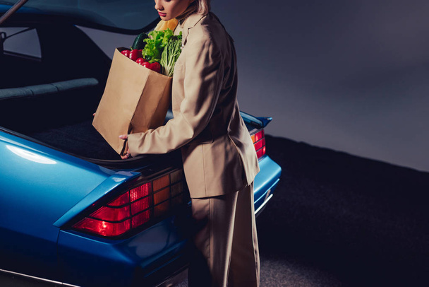 oříznutý pohled stylové ženy v obleku balení papírové tašky s jídlem v kufru  - Fotografie, Obrázek