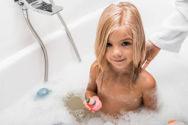 overhead view of cute child taking bath and holding rubber toy near mother  - Photo, Image
