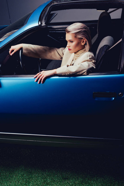 wysoki kąt widzenia atrakcyjnej i stylowej kobiety w garniturze siedzi w samochodzie retro  - Zdjęcie, obraz