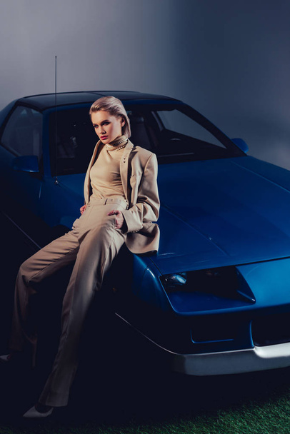attractive and stylish woman in suit sitting on retro car  - Фото, изображение