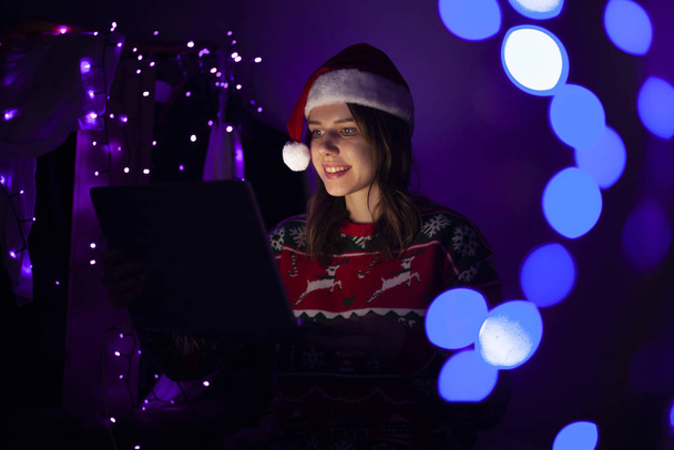 girl student in Christmas clothes sits at home with a laptop at night, a lonely woman meets a holiday online, she use a computer for Christmas - Foto, Imagen