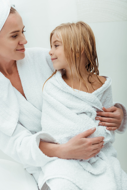 happy mother looking at cute and wet daughter in bathroom  - Фото, зображення