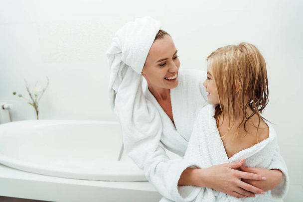 щаслива мати посміхається, дивлячись на дочку у ванній
  - Фото, зображення