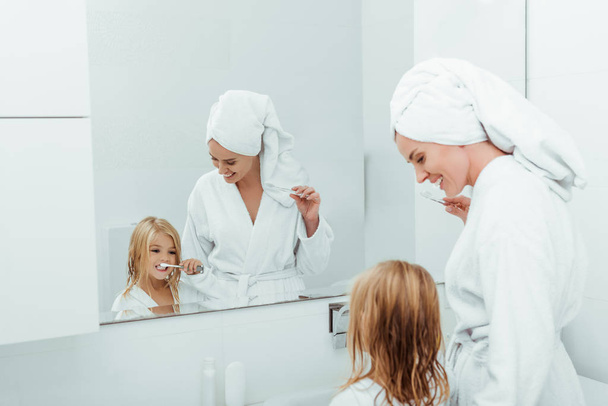 feliz madre mirando hija cepillarse los dientes cerca del espejo
  - Foto, Imagen