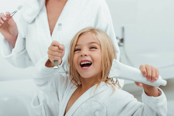 selective focus of happy kid holding toothpaste near mother  - Fotó, kép