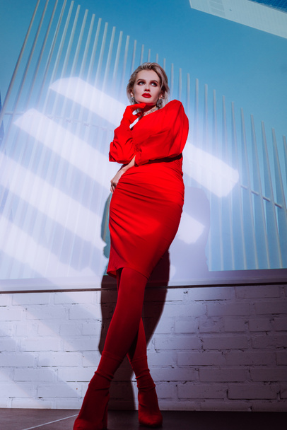 χαμηλή γωνία άποψη του ελκυστική και κομψή γυναίκα σε κόκκινο φόρεμα στο φόντο της πόλης  - Φωτογραφία, εικόνα
