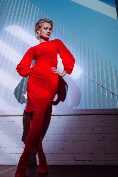 魅力的でスタイリッシュな女性の低角度ビューの赤いドレスに手で街の背景に腰  - 写真・画像