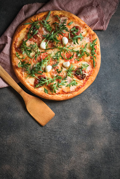 ハム、キノコ、アルグラ、モッツァレラ、バジル、トマトと伝統的なイタリアのピザ暗い背景のトップビューコピースペース. - 写真・画像