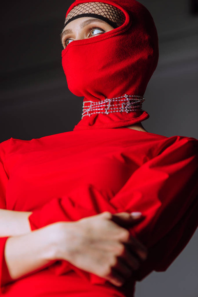 low angle view of stylish woman in red dress and balaclava isolated on grey - Foto, Imagem