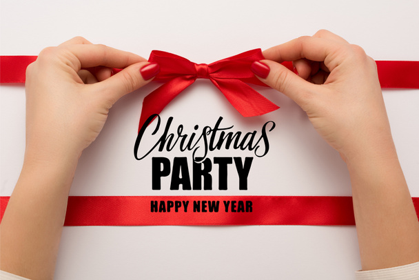 cropped view of woman touching red bow near christmas party, happy new year lettering on white  - Foto, Imagem