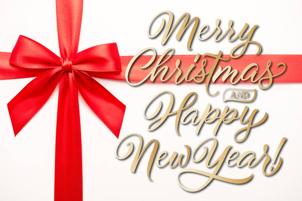 vue du haut du ruban avec noeud en satin rouge près de joyeux Noël et bonnes lettres de nouvelle année sur blanc
  - Photo, image