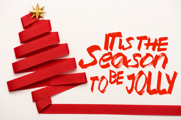 top view of red ribbon with star shape bow near its the season to be jolly letters on white  - Photo, Image
