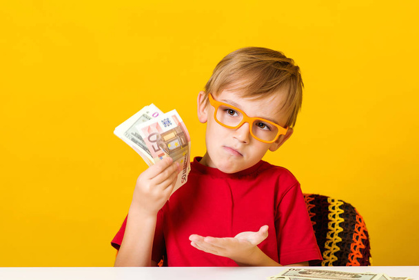 Kind mit Brille, das darüber nachdenkt, wo man Geld anlegen sollte, um Gewinn zu machen. Finanzielle Alphabetisierung von Kindern - Foto, Bild