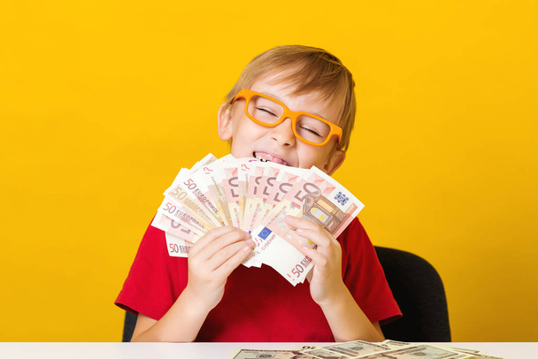 Excited boy in glasses with a fan of money. Future savings. Financial literacy of children. Kid thinking where to invest money - Photo, Image