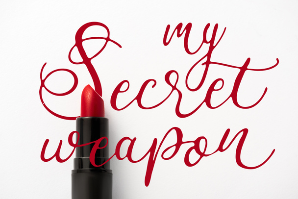 Draufsicht auf schwarze Tube mit rotem Lippenstift in der Nähe meiner Geheimwaffe Buchstaben auf Weiß  - Foto, Bild