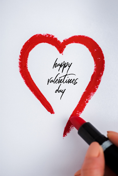 abgeschnittene Ansicht einer Frau, die Herz mit rotem Lippenstift zeichnet, in der Nähe von glücklichen Valentinstagen Buchstaben auf Weiß  - Foto, Bild