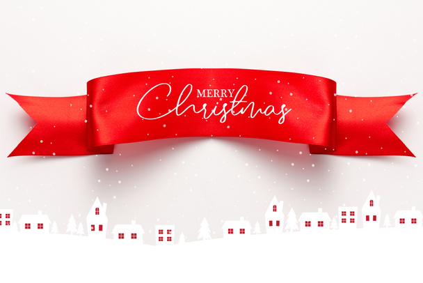 top view of red satin ribbon with merry christmas lettering near houses and pines on white  - Photo, Image