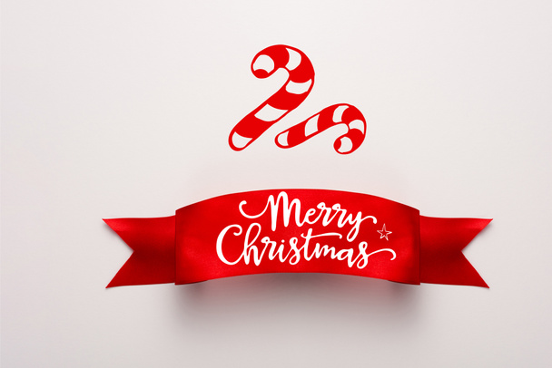 vista superior de la cinta roja con tipografía navideña alegre cerca de bastones de caramelo en blanco
  - Foto, imagen