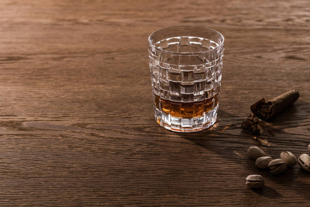 Glas cognac met sigaar en pistachenoten op houten tafel - Foto, afbeelding