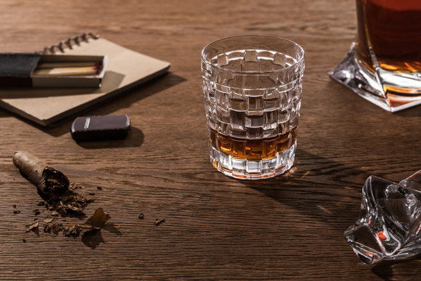 Brandy in glass and decanter with cigar, lighter and matches on wooden table - Fotoğraf, Görsel