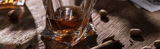 Sklenice brandy s doutníkem a pistáciemi na dřevěném stole, panoramatický výstřel - Fotografie, Obrázek