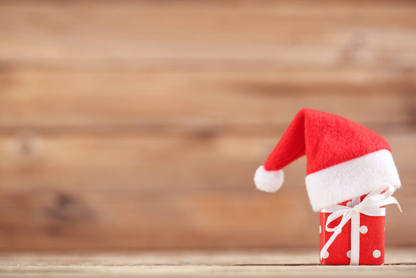 Kahverengi ahşap arka planda hediye kutusu olan kırmızı Noel Baba şapkası. - Fotoğraf, Görsel
