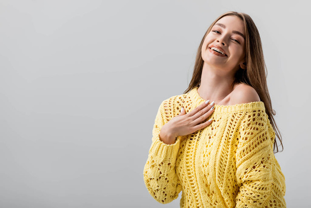 beautiful girl laughing at camera while holding hand on chest isolated on grey - Fotoğraf, Görsel