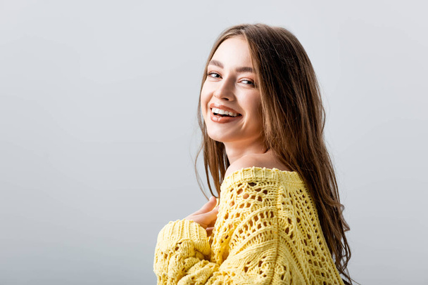 cheerful girl looking at camera while holding hand on chest isolated on grey - Fotografie, Obrázek