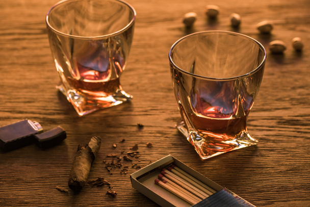 Gläser Brandy mit Zigarre, Feuerzeug und Pistazien auf Holztisch - Foto, Bild