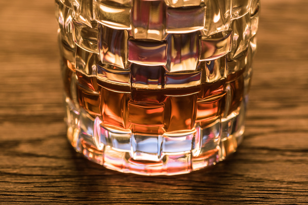 Close-up zicht van brandy in getextureerd glas op houten tafel - Foto, afbeelding