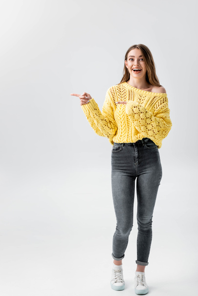 full length view of cheerful girl pointing with fingers and looking at camera isolated on grey - Foto, Imagem