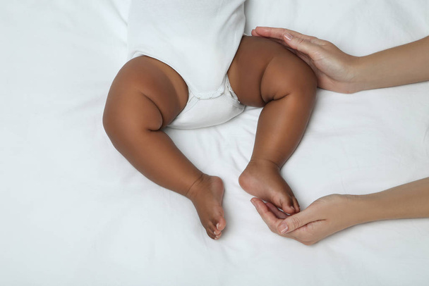 American baby girl lying on white bed with mother hands - Photo, image