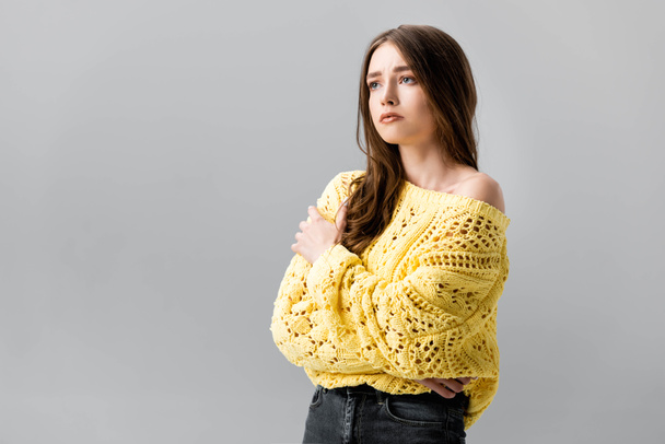 smutna dziewczyna w żółtym swetrze stojąca z skrzyżowanymi ramionami i patrząca odizolowana na szaro - Zdjęcie, obraz