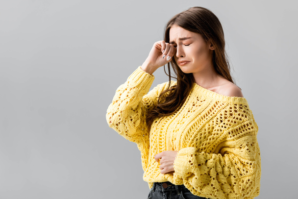 unhappy girl in yellow sweater crying and wiping tears with hand isolated on grey - Photo, Image