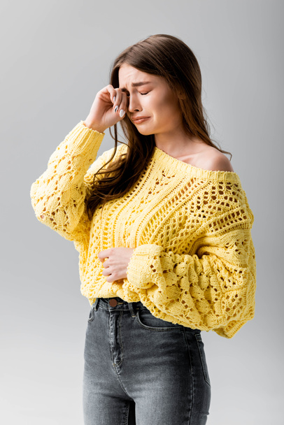 offended girl in yellow sweater crying and wiping tears with hand isolated on grey - Photo, Image