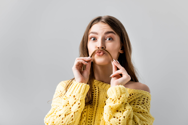 tricky girl in yellow sweater holding hair above lip like mustache isolated on grey - Photo, image