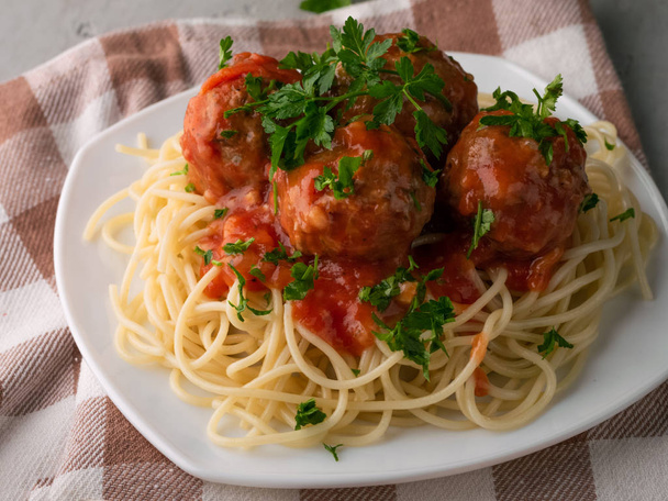 Крупним планом приготовані спагетті з фрикадельками в томатному соусі на картатому ватному столі-накидку на дерев'яному фоні
 - Фото, зображення