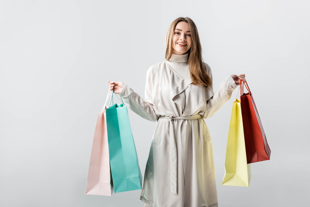 cheerful, stylish girl looking at camera while holding shopping bags isolated on grey - Foto, immagini