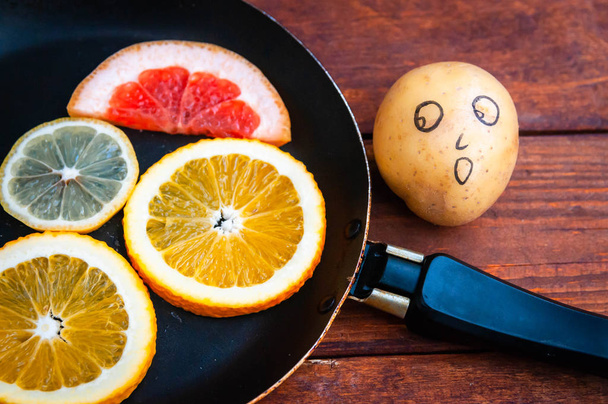 potato with an emotional face looks at citruses. - Foto, Imagem