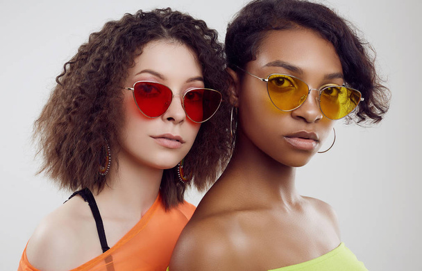 Kaksi nuorta kaunista hipsterityttöä kesävaatteissa ja kirkkaissa aurinkolaseissa
 - Valokuva, kuva