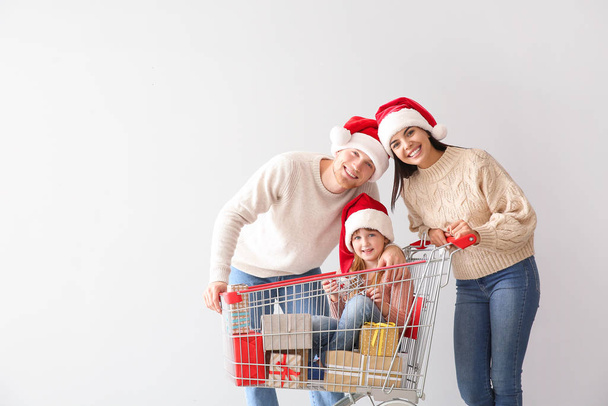 Familie mit Einkaufswagen voller Weihnachtsgeschenke auf hellem Hintergrund - Foto, Bild