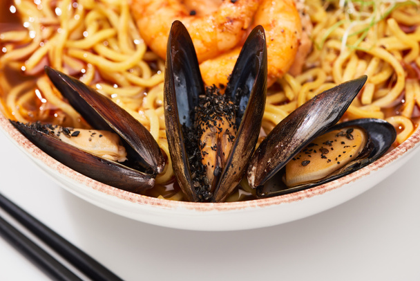 close up view of spicy seafood ramen in bowl with mussels near chopsticks - Foto, afbeelding