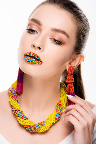 attractive girl in beaded accessories, with beads on lips, touching earring isolated on white - Fotó, kép