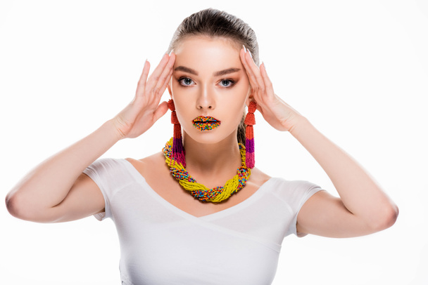 beautiful girl in beaded accessories, with beads on lips, touching head and looking at camera isolated on white - Photo, Image