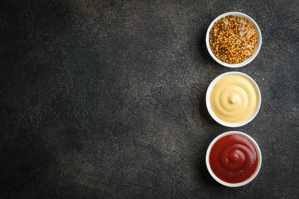Set beliebter Soßen - Senf, Ketchup und Mayonnaise auf dunklem Hintergrund. Ansicht von oben freier Kopierraum. - Foto, Bild